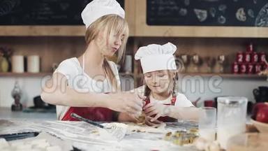 妈妈和女儿穿着同样的衣服，在舒适的厨房里准备面团，玩得很开心。 烹饪，妈妈和女儿的概念