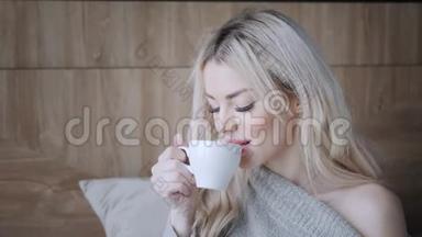 美丽<strong>的</strong>金发女人拿着陶瓷杯<strong>的</strong>茶或咖啡享受。 在床上<strong>喝茶</strong>。 看着窗户<strong>喝茶</strong>