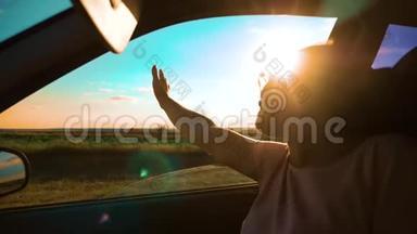 女孩挥手在窗户阳光下，风在汽车慢动作视频。 年轻快乐的女孩开汽车