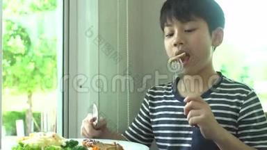 小亚洲男孩在餐厅吃牛排和蔬菜沙拉，微笑着面对