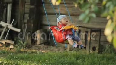 可爱的小男孩在夏天的花园里玩秋千。 树上挂着一圈圈