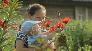 年轻的母亲和她美丽的男孩在他家附近抚摸鲜花。儿子<strong>聚精会神</strong>地看着这些植物