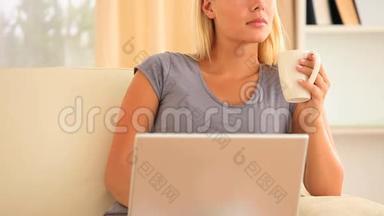女人一边拿着一杯咖啡坐在沙发上一边拿着笔记本，一边想着