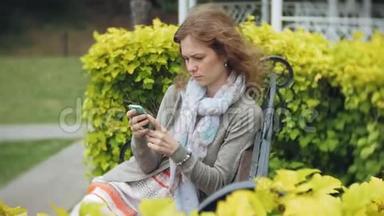 在<strong>美丽</strong>的绿色公园的长凳上使用智能手机放松的女人。 <strong>校园</strong>中的年轻千禧妇女做手势