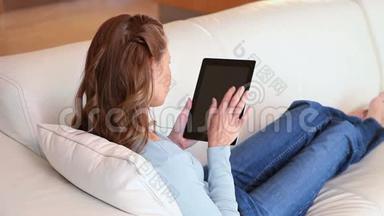 一个女人躺在沙发上，手里拿着平板电脑