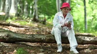 女人坐在森林中的一棵倒下的树上，用智能手机