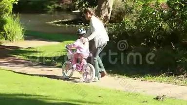 微笑的<strong>女人帮</strong>助她的女儿骑自行车