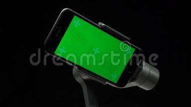 智能手机上带有绿色屏幕的步进式万向节稳定器正在旋转。
