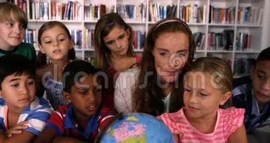 教师协助学童在图书馆阅读地球仪