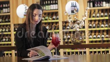 一个年轻女孩在一家时尚餐厅的桌子上喝一杯鸡尾酒，一个年轻女孩在一张桌子上喝一杯红色异国情调的鸡尾酒。