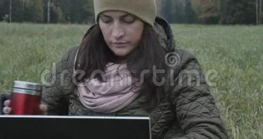 年轻的深色头发的女学生在大自然中做<strong>笔记本</strong>电脑。 美丽的秋日和女人在使用<strong>笔记本</strong>电脑时享受它。