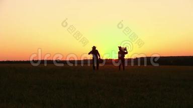 两个农民拿着铲子走在田野上。 他们携带种植树木的设备。 在日落的时候。 侧视图