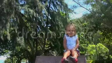漂亮的小宝宝坐在花岗岩基座上，<strong>环顾四周</strong>。 她微笑着，挺直了头发。 在背景树中