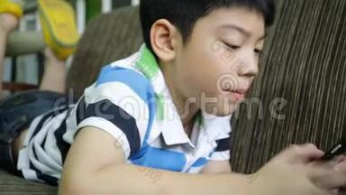 亚洲孩子在家里躺在沙发上用<strong>数码手机</strong>。