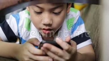 亚洲孩子在家里躺在沙发上用<strong>数码手机</strong>。
