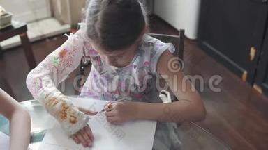 带着绷带的断臂的孩子用<strong>彩色铅笔画</strong>画。 手受伤的小女孩。