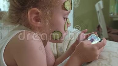 一个漂亮的小女孩兴高采烈地在家里制作黄瓜面具，并使用智能手机