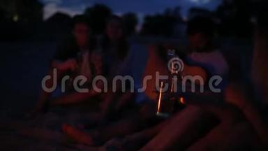 日落海滩派对，篝火晚会。 朋友们<strong>围坐</strong>在篝火旁，喝着啤酒，对着吉他唱歌。 青年