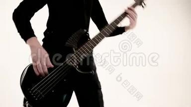 年轻的男音乐家穿着黑色衣服，白色背景上有一把黑色低音吉他。 低音吉他演奏者演奏音乐
