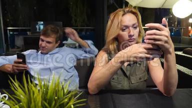 一对情侣在户外咖啡馆谈恋爱。 男人和美女约会。 所有人都在看他的手机，4K，