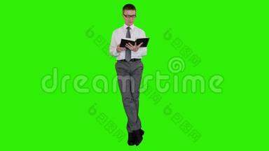 年轻的商人戴着眼镜看着一本书坐着，绿色屏幕，股票录像