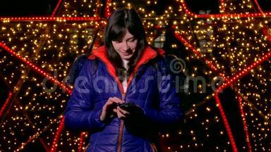 女孩拿着智能手机看社交媒体的夜晚，在博克的冬日灯光下