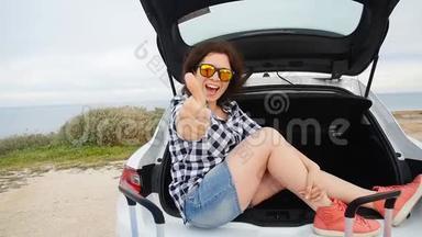 快乐的年轻女子暑假坐在汽车后备箱里