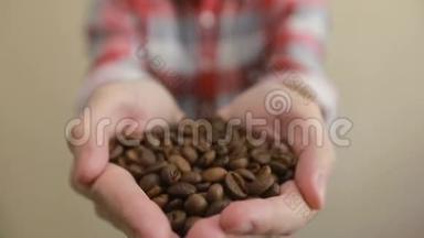 咖啡豆-男人展示中等烤咖啡豆一把。 手里拿着咖啡豆的男人
