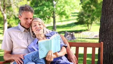 坐在公园长椅上看书的一对恩爱的夫妇