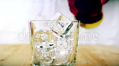 酒吧老板把威士忌倒在杯子里，在木桌背景上放冰块，专注于冰块，威士忌放松时间，黄金温暖