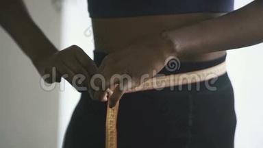 在家穿运动服装的年轻黑人妇女的特写镜头，美国黑人女孩用黄色胶带测量腰部