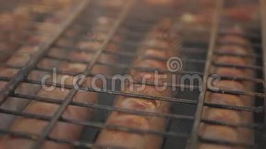 在烧烤架上烤香肠。 将猪肉香肠烤在带有香肠的便携式烤架上，靠近烤架，肉