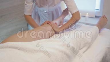 年轻女子在美容院做脚部按摩。 玛瑟用蜡烛揉捏一个年轻漂亮女孩的脚和腿