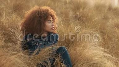 黑色混血女人，大非洲卷发，在草地上，高干的秋草和日落光