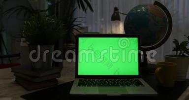 带有绿色屏幕的笔记本电脑。 黑暗的办公室。 多莉<strong>向左向</strong>右移动。 完美地放置你自己的图像或视频。 技术绿屏