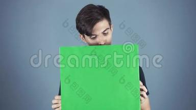 好奇的年轻人穿着黑色衬衫，拿着绿色的钥匙片海报，灰色的背景