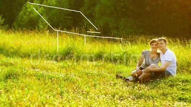 年轻幸福的夫妇坐在公园的绿草地上，梦想着拥有自己的房子。抵押概念。