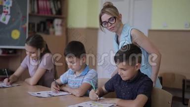 老师在课堂上帮助学校的孩子写作测试。 教育、小学、学习和人的概念
