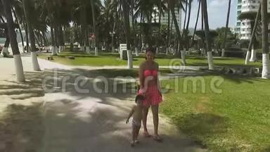 年轻漂亮的女人穿着粉红色的泳衣，带着一个婴儿在公园和瓦维的背景下漫步在水边