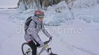 女人正在冰窟附近骑自行车。 有冰洞和冰柱的岩石非常美丽。 女孩穿着