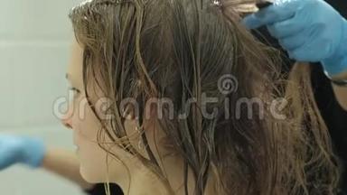 女理发师在家里的浴室里给一个年轻女人的头发涂上油漆，用刷子涂上油漆