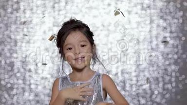 可爱快乐的小女孩穿着银色的裙子在银色的背景下跳舞。
