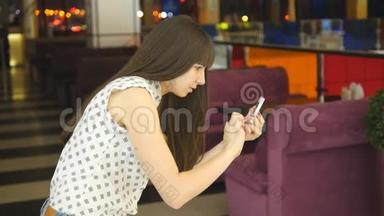 年轻女子在购物中心玩室内游戏，使用智能手机。 女孩玩流行的智能手机游戏-捕捉