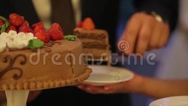 新娘和新郎的手切一片婚礼蛋糕。 切结婚蛋糕。 人们切蛋糕，把蛋糕放在盘子里