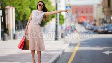 带着购物袋的年轻快乐的女孩<strong>坐出租车</strong>。 站在大街上举着一个美丽幸福的女人的肖像