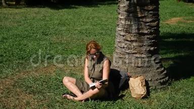 金发女人在公园里看书，坐在草地上，树下。 4k，慢镜头