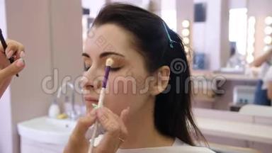 双手化妆师将化妆涂在一个年轻女人的脸上。 在专业沙龙里做眼妆的<strong>女孩</strong>。 晚上