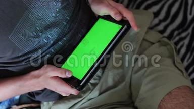 男人拿着一台空白平板电脑，沙发上有绿色屏幕