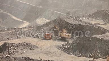 挖土机和翻斗车在采石场里，大型黄色挖掘机把矿石装进翻斗车里