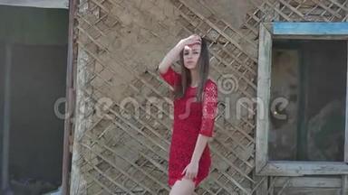 穿红色裙子的漂亮女孩。 穿裙子的女孩站在废墟的旧房子旁边，生活方式